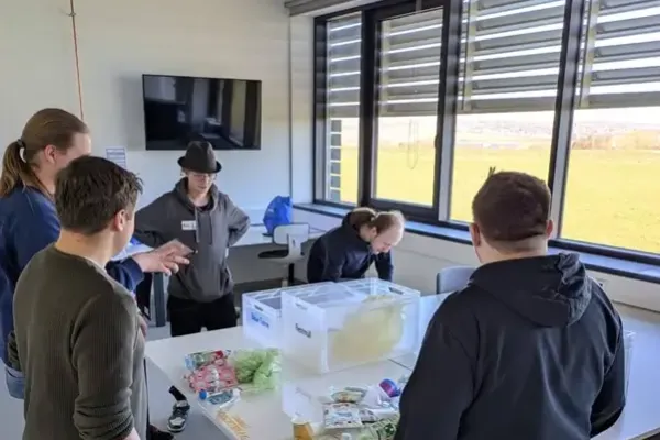 Eine Gruppe von Schülern steht um einen Tisch im SKZ-Labor und hört einer Betreuerin zu, die ihnen Materialien und Experimente zum Thema Kunststoffe und Nachhaltigkeit erklärt.