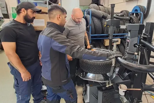 Drei Auszubildende beobachten eine Reifenmontage an einer Montiermaschine.