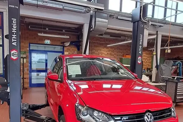 Ein rotes Auto steht auf einer Hebebühne in einer Werkstatt.
