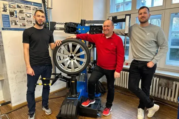 Drei Lehrkräfte stehen lächelnd neben einer Reifenmontiermaschine mit montiertem Reifen.