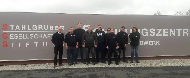 Sieben Teilnehmer der Fortbildung im Vulkaniseur-Handwerk stehen vor dem Schild des Schulungszentrums der STAHLGRUBER GESELLSCHAFTER-STIFTUNG in Warstein-Belecke.